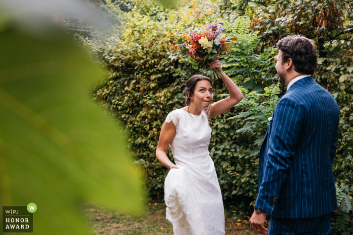 Antwerpen outdoor, garden wedding photo from Flanders at the bride and groom's house showing the bride is taking shelter under her bouquet