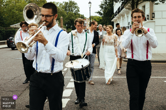 Foto di reportage di matrimonio in Inghilterra da Chelsea, Londra, mentre gli sposi e la band camminano per le strade fino al ricevimento