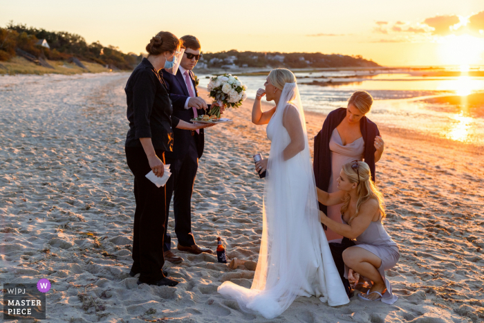 Strandhuwelijksfoto van Massachusetts van Brewster MA van de bruidsmeisjes terwijl ze de jurk van de bruid bezighouden