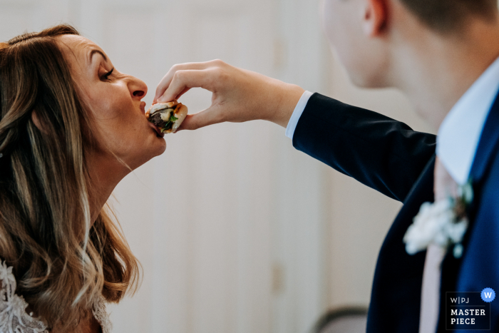 Dunedin, Hull wedding image of the bride being fed a burger by her step son so she doesn't get any food on her dress in East Yorkshire Dunedin, Hull wedding image of the bride being fed a burger by her step son so she doesn't get any food on her dress in East Yorkshire