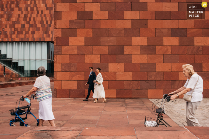 Fotografia di matrimonio di Antwerpen della sposa e dello sposo che passano accanto a due vecchie signore in città lungo la strada