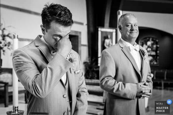 Foto di matrimonio in Pennsylvania della reazione dello sposo nel vedere la sua sposa entrare in chiesa mentre suo padre / testimone prende tutto.