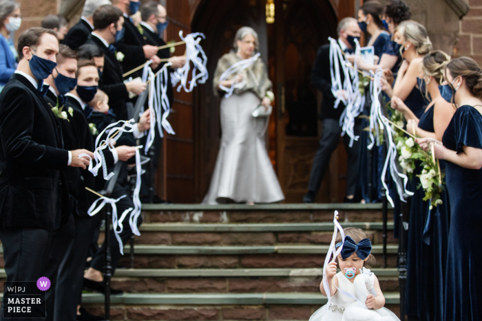 Fotografía de boda de la Universidad de Seton Hall Chapel, Nueva Jersey: la niña de las flores se para frente a la multitud antes de que los novios salgan de la iglesia