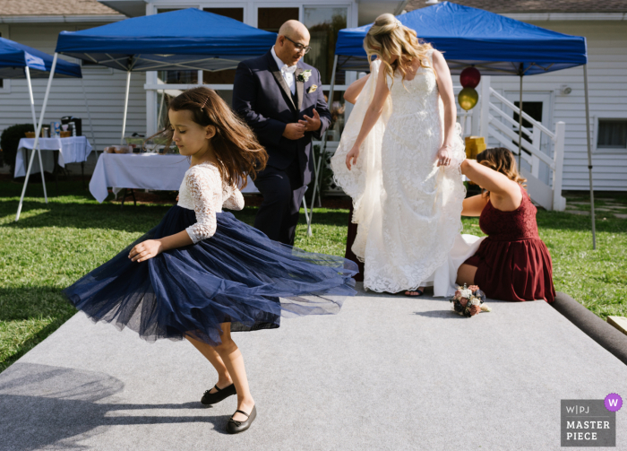 Schenectady, NY wedding photographer captured a little flower girl spinning in her dress while behind her the bride's dress is being bustled by her bridesmaids and her new husband stands by