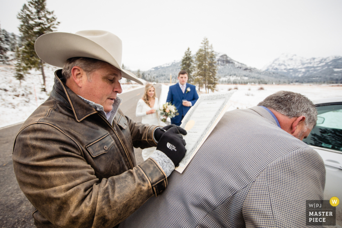 Zdjęcie ślubne z Yellowstone przedstawiające ojca panny młodej korzystającego z pleców ojca pana młodego do wypełnienia aktu małżeństwa