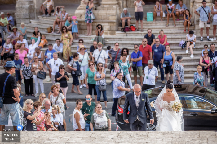 Trouwfoto's van de kerk op Sicilië van de bruid die de trap opkomt voor de ceremonie met een grote groep toeristen die toekijkt