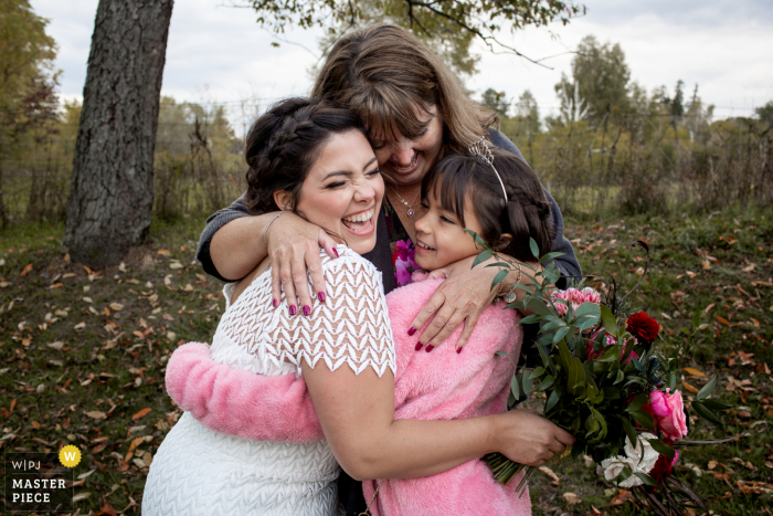 Foto de boda en Ontario Backyard que muestra a la novia recibiendo abrazos de su tía y sobrina después de la ceremonia