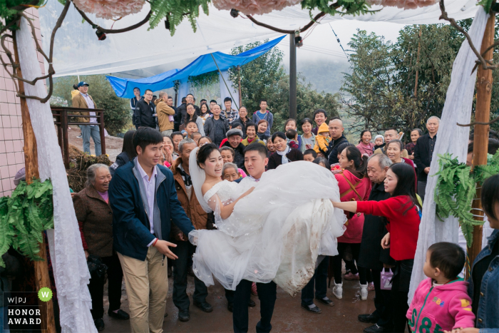 Fotograf ślubny ChongQing rejestruje oblubieńca niosącego pannę młodą do nowego domu, przyciągając wieśniaków do oglądania