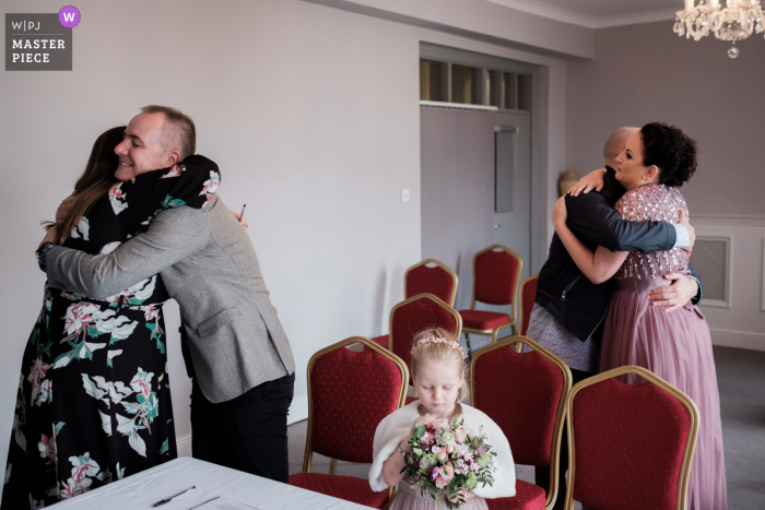 Fotografia de casamento do Royal Hotel, Bray, Irlanda mostrando a filha permanece fascinada por seu buquê, mesmo após o término da cerimônia, quando os dois abraçam suas testemunhas