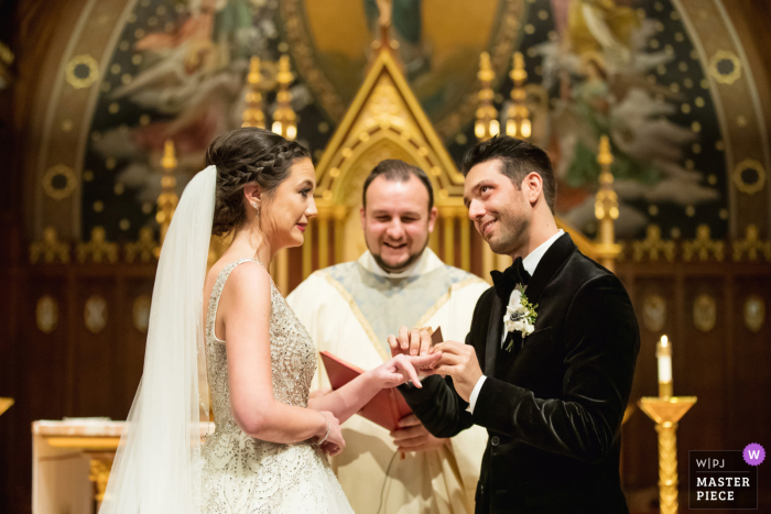 Seton Hall Chapel, Seton Hall University, New Jersey wedding photo created as the groom struggles to get ring on bride 