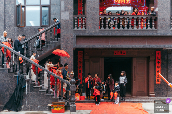 Fotografía de la boda en casa de Fujian de la fiesta nupcial completa bajando las escaleras con un paraguas rojo