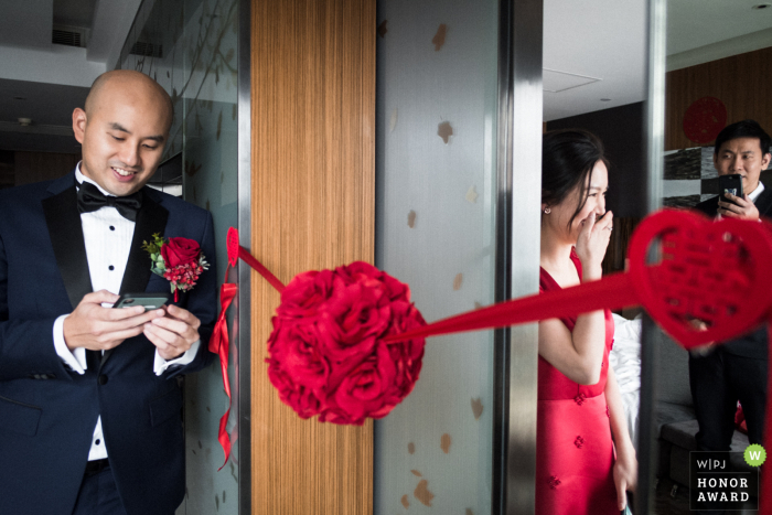 HK trouwfoto van Hotel Icon, Hong Kong of the Bride, verstopt in de kamer, reageert terwijl de bruidegom de 'liefdesverklaring' voorleest, voordat hij de bruid voor de eerste keer ontmoet. De broer van de bruid kijkt toe en filmt met zijn telefoon, zoals weerspiegeld