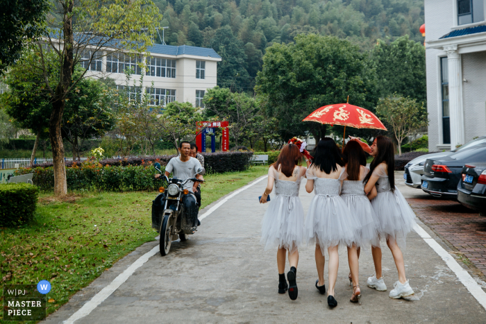 Fujian, China huwelijksfotografie van bruidsmeisjes die buiten lopen onder een rode paraplu