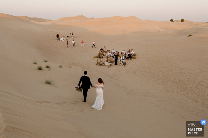 Dubai Desert-huwelijksfotografie van het paar dat over het zand loopt bij Returning to the desert reception