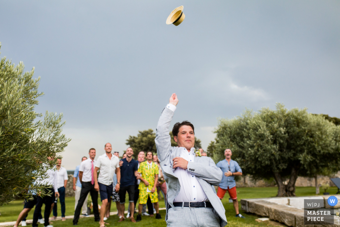 Vin d'honneur Hochzeitsfotografie des Bräutigams, der den Männern im Freien seinen Hut wirft