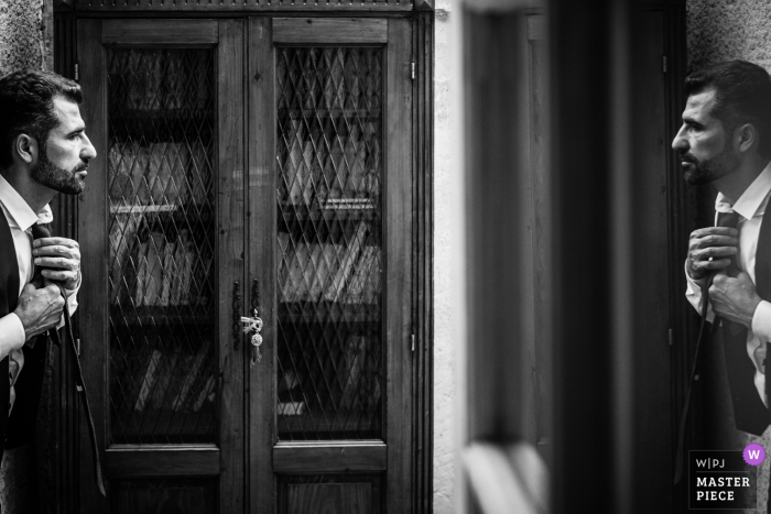 France home wedding photography of the groom working in a mirror to tie it up France home wedding photography of the groom working in a mirror to tie it up