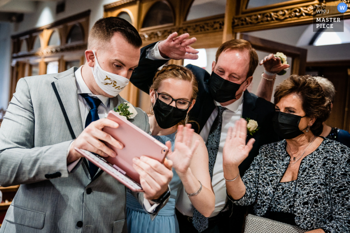 Pennsylvania Ceremony wedding photography showing Sign of the times as the groom gets a livestream set up for the ceremony about to start, his family comes over to say hello to the extended family that couldn't be there in person because of Covid restrict Pennsylvania Ceremony wedding photography showing Sign of the times as the groom gets a livestream set up for the ceremony about to start, his family comes over to say hello to the extended family that couldn't be there in person because of Covid restrict