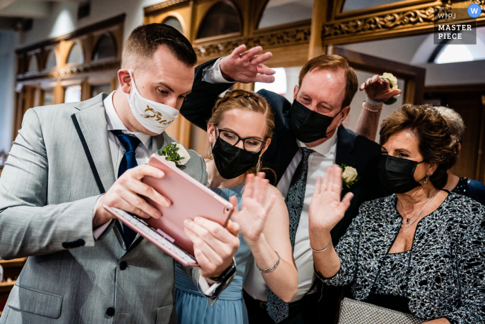 Pennsylvania Ceremony huwelijksfotografie toont Sign of the Times terwijl de bruidegom een ​​livestream krijgt voor de ceremonie die op het punt staat te beginnen, zijn familie komt langs om hallo te zeggen tegen de uitgebreide familie die er niet persoonlijk kon zijn vanwege Covid-beperking