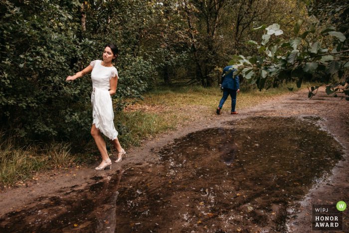 Fotografia de casamento na Antuérpia perto do local da recepção enquanto a noiva tenta passar por uma poça que está bloqueando a estrada, enquanto o marido já desistiu e está indo em direção ao outro lado