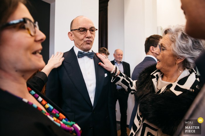 Trouwfoto van het stadhuis in Vlaanderen waarop 2 vrouwen het vest van een echtgenoot controleren