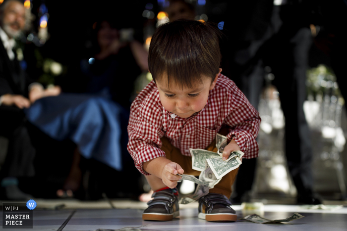 Seawell Ballroom wedding photo showing A young boy picking up dollar bills off the dance floor during a greek wedding