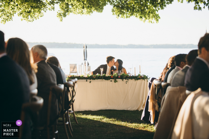 Photographie de mariage à Chicago depuis la réception en plein air du couple s'embrassant au bord de l'eau sous les arbres