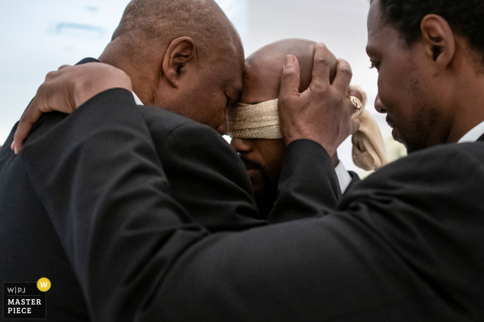 Huwelijksfoto van een ceremonie in New Jersey waarop de vader in gebed omhelst met zoon en broer