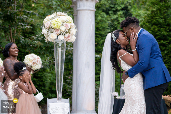 Outdoor Delaware garden ceremony photo of the couple kiss with flower girl who can't take the PDA