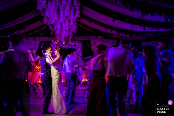 A UK wedding reportage photographer in London created this image of the Bride and Groom dancing under purple lights at the reception party