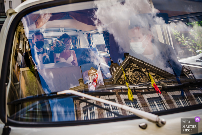 A wedding photographer in Limburg created this image of the couple waiting inside a vintage van outside the building