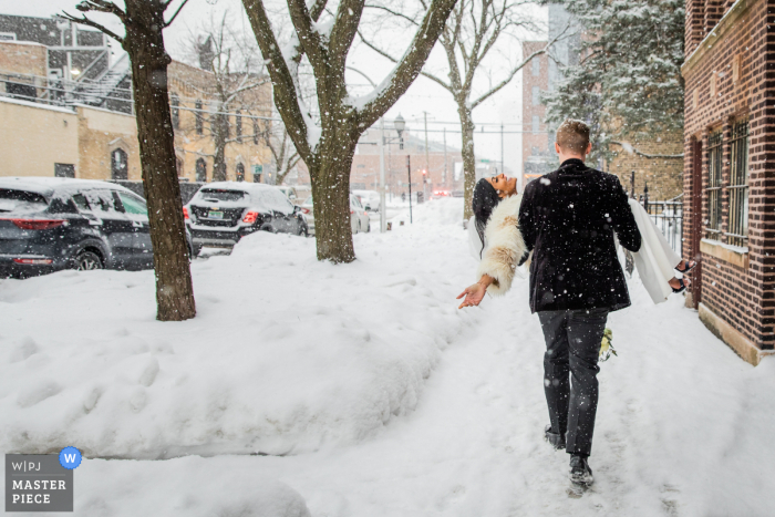 Der Hochzeitsfotograf aus Illinois hat dieses Bild des Bräutigams geschaffen, der die Braut hält, während sie durch den Winterschnee zurück in ihre Wohnung für ihren Empfang stapfen