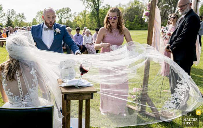 Ein Top-Hochzeitsfotograf in Raymore, Missouri, hat dieses Bild eines sehr langen Schleiers aufgenommen, ein Herzstück ihrer Hochzeitskleidung, das in jeder Hinsicht reizend war, außer dass ein Wind auffrischte und der Kommunionbecher überschwappte