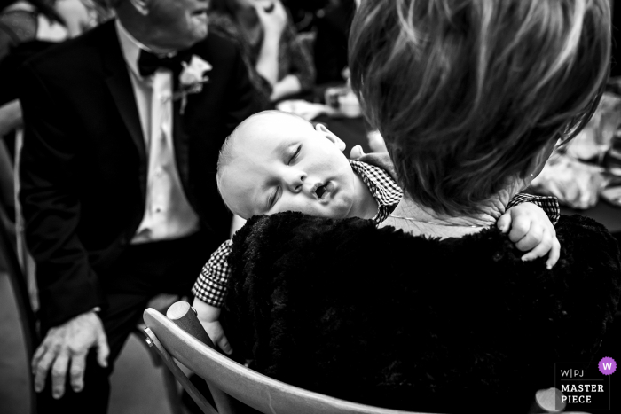 Um fotógrafo de casamento em Spring, TX criou esta imagem no local de casamento e eventos Addison Woods de um bebê tirando uma soneca no ombro da vovó durante a recepção