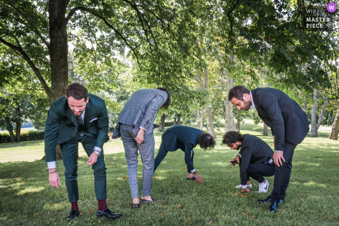 Un importante fotógrafo de bodas de Francia en el Château Saint Loup en Albret capturó esta imagen del novio y los padrinos de boda buscando en la hierba bajo los árboles un objeto desconocido.