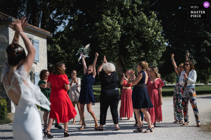 Fotograf ślubny z Francji w Domaine de Pécarrère stworzył ten obraz panny młodej rzucającej bukiet kobietom na zewnątrz