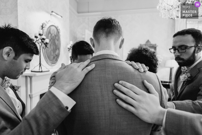 A San Antonio wedding photographer at The Argyle created this image of The groom with his back to the camera holds a prayer with groomsmen