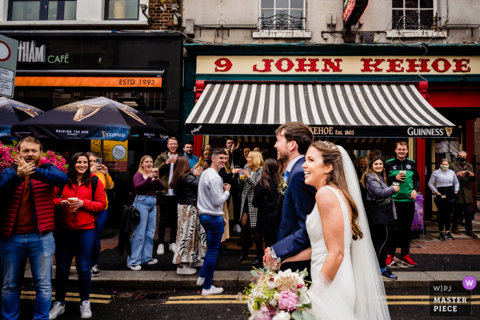 La migliore fotografia di reportage di matrimonio della città di Dublino in Irlanda che mostra una foto di una folla di festaioli che bevono all'aperto durante le regole di Covid reagiscono al vedere gli sposi novelli