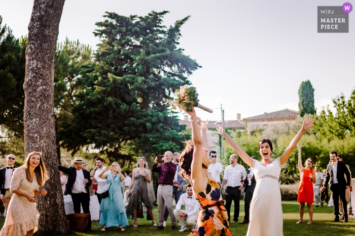 Ein Top-Hochzeitsfotograf in Herault hat dieses Bild auf der Domaine Fon de Rey im Freien aufgenommen, das das Werfen eines Blumenstraußes bei einer Hochzeit zeigt