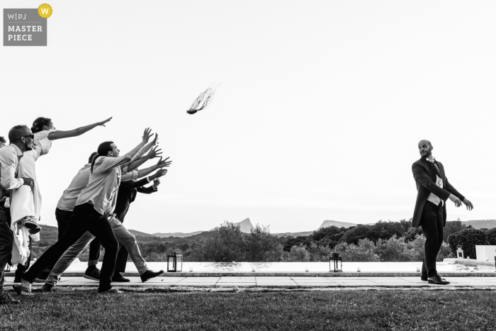 Un grand photographe de mariage au Mas Saint Germain en France a capturé cette photo en BW montrant Le marié lance une manette de jeu aux hommes célibataires