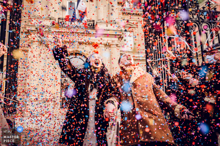 A wedding photographer at the Paris City Hall created this image showing Bride and groom are going out of the city hall, guests are throwing confetti  