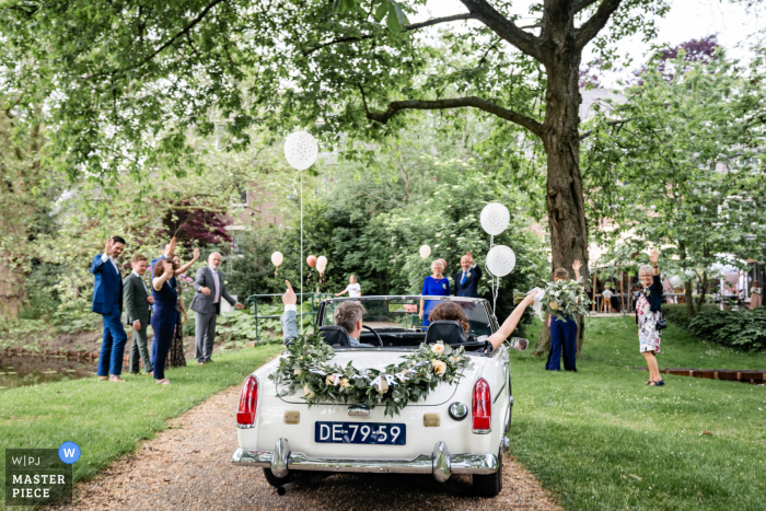 A wedding photographer in Alphen aan den Rijn created this image of the bride and groom waving goodbye after the wedding as they drive away in convertible car