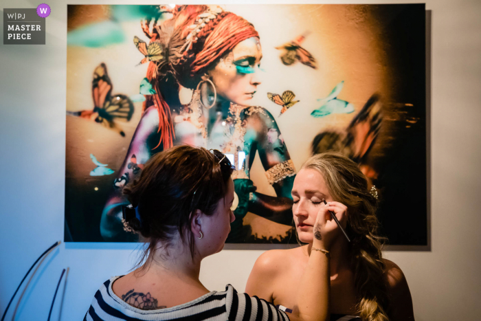 A top wedding photographer in Noord Brabant captured this picture of the bride getting ready near a painting on the wall