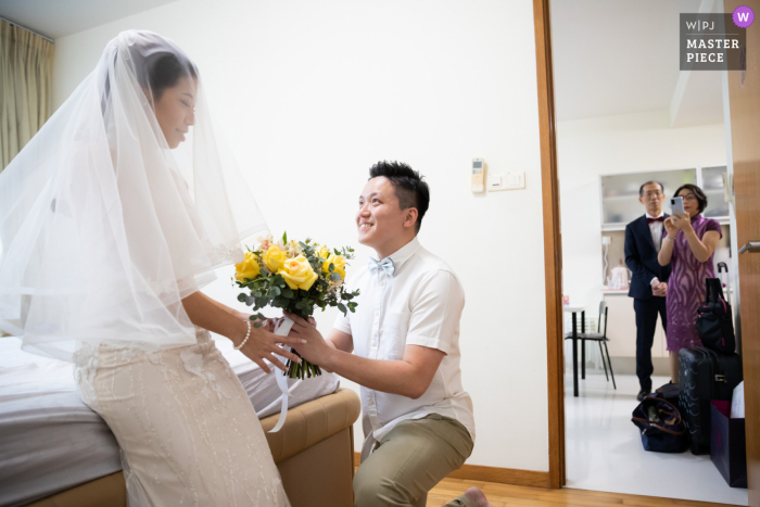 Een huwelijksfotograaf in Singapore maakte dit beeld van de bruidegom die het boeket aan zijn bruid presenteert terwijl haar ouders toekeken