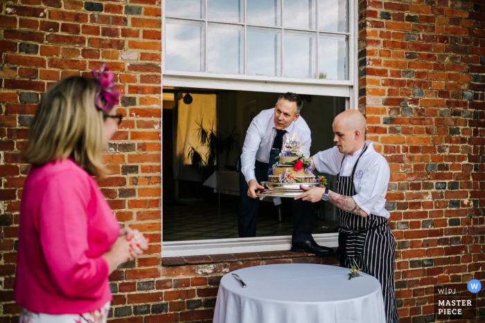 A UK wedding photographer at Rownhams House created this image of The caterers bringing the cake out a window