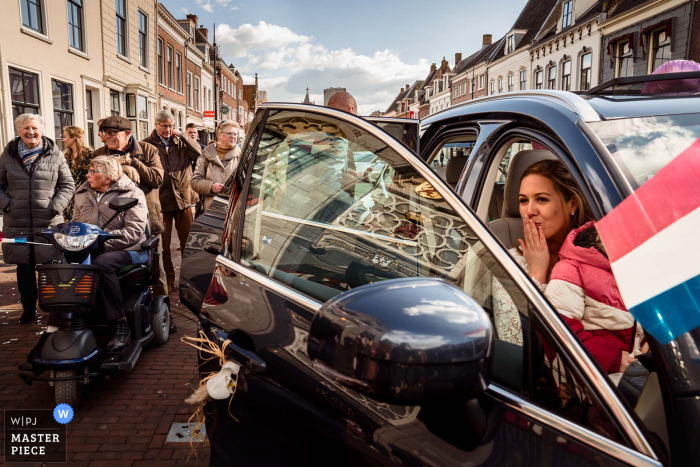 Een Nederlandse top huwelijksfotograaf in Vianen, net buiten het stadhuis, maakte deze foto van De bruid die een handkus geeft aan iemand in het publiek terwijl iedereen zijn huwelijk viert