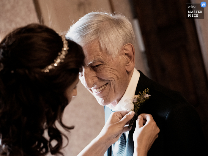 Une photo de mariage de Castello di Cernusco à Lombardone capturant cette photo de la mariée épinglant la fleur dans sa boutonnière à son père, il la regarde fasciné