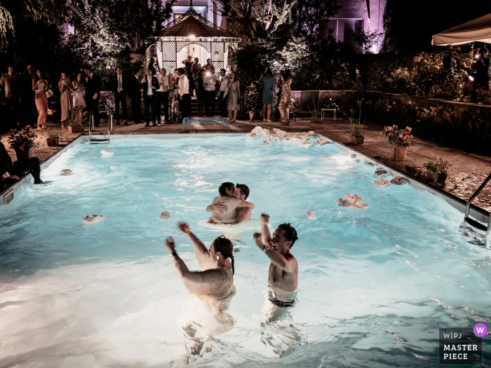 Een top huwelijksfotograaf in Casalpusterlengo maakte deze foto waarop te zien is dat het huwelijksfeest bijna voorbij is en de bruid en bruidegom kussen in het zwembad, uitgeput maar gelukkig