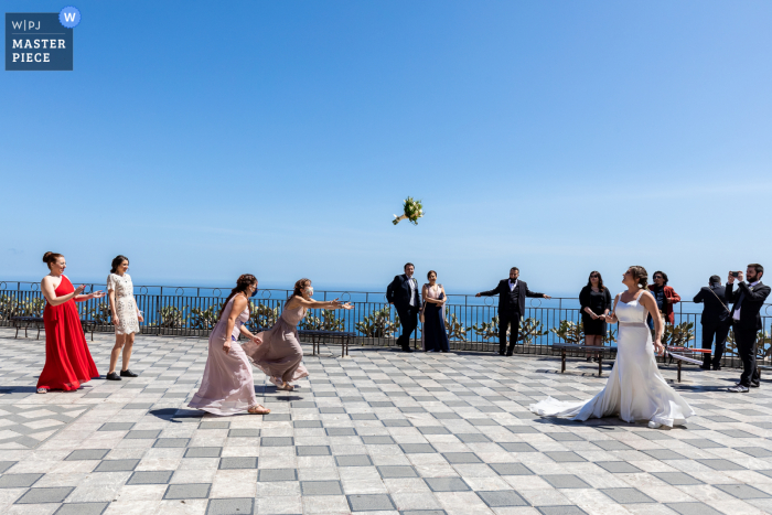 Ein italienischer Hochzeitsfotograf auf der Piazza IX Aprile in Taormina hat dieses Bild einer Braut geschaffen, die alleinstehenden Frauen einen Blumenstrauß im Freien am Meer zuwirft Ein italienischer Hochzeitsfotograf auf der Piazza IX Aprile in Taormina hat dieses Bild einer Braut geschaffen, die alleinstehenden Frauen einen Blumenstrauß im Freien am Meer zuwirft