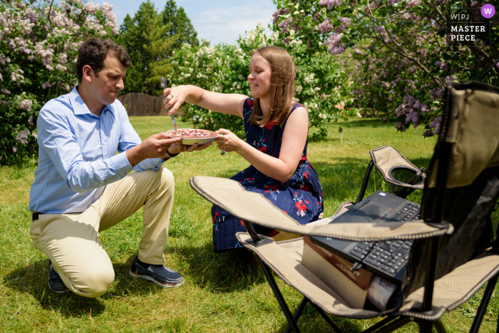 Un destacado fotógrafo de bodas en el Jardín Botánico de Montreal capturó esta imagen de una pareja de novios cortando un pastel frente a una computadora portátil en medio de un jardín.