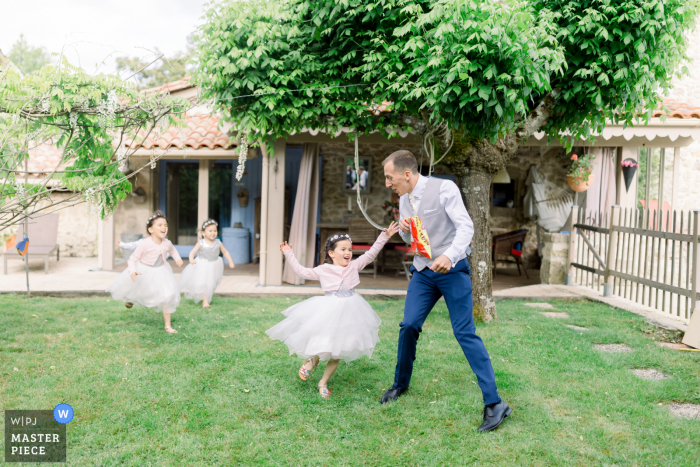 Ein Hochzeitsfotograf aus Bordeaux, Frankreich, hat dieses Bild des Bräutigams kreiert, der während des Gartenempfangs im Freien mit Kindern spielt